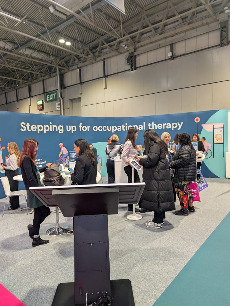 Photo of RCOT colleagues talking to people at the OT Show. Stand says 'Stepping up for occupational therapy'.