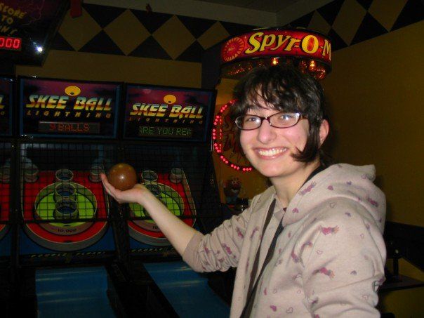 Picture of Grailytoast circa 2006 smiling, with bangs, in front of a skeeball machine, holding a skeeball.