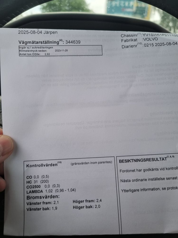 Bilden visar ett besiktningsprotokoll som hålls upp framför ratten på en Volvo V70 från 2001. Inga anmärkningar vilket ger 14 månader till att använda bilen lagligt. Har ägt denna bil i 19 år nu. Den vill verkligen leva vidare i familjen.
