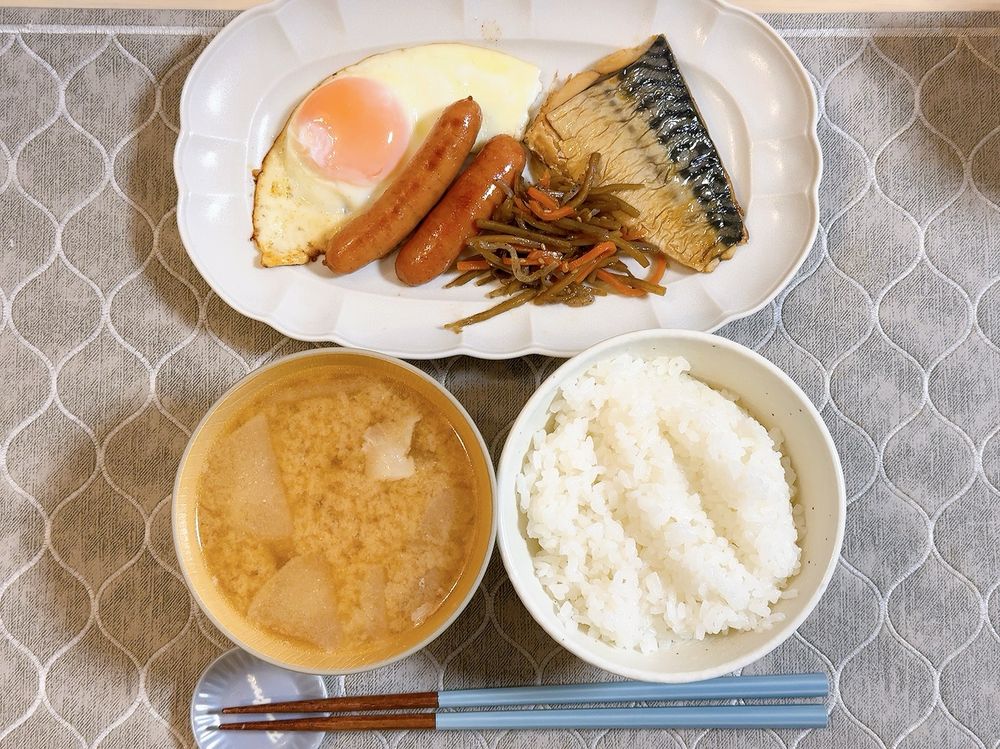食卓に鯖の塩焼き、目玉焼き、焼いたウィンナー、きんぴらごぼう、豚汁、白ご飯が配膳されている