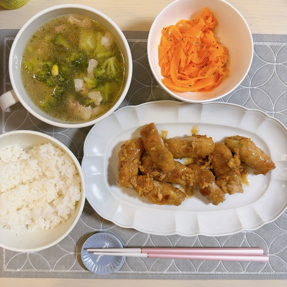 食卓に豚肉の大葉チーズ巻き、にんじんのラペサラダ、ブロッコリーとベーコンのコンソメスープ、白ご飯が配膳されている