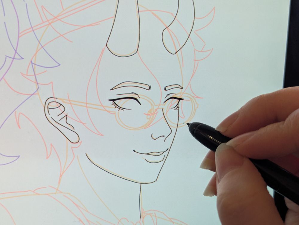 A photo of a tablet screen with a hand holding a pen, drawing lineart for a sketch of a demon vtuber.