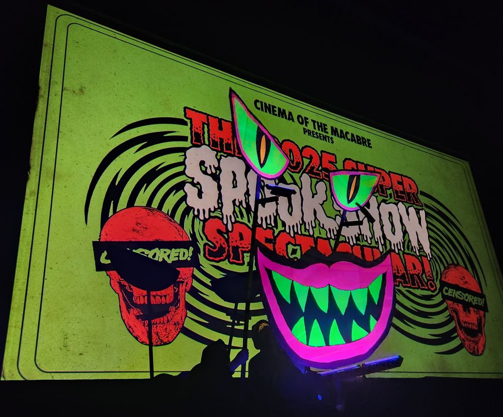 Cinema of the Macabre presents the 2025 Super Spookshow Spectacular with a blacklit demon face smiling at the crowd
