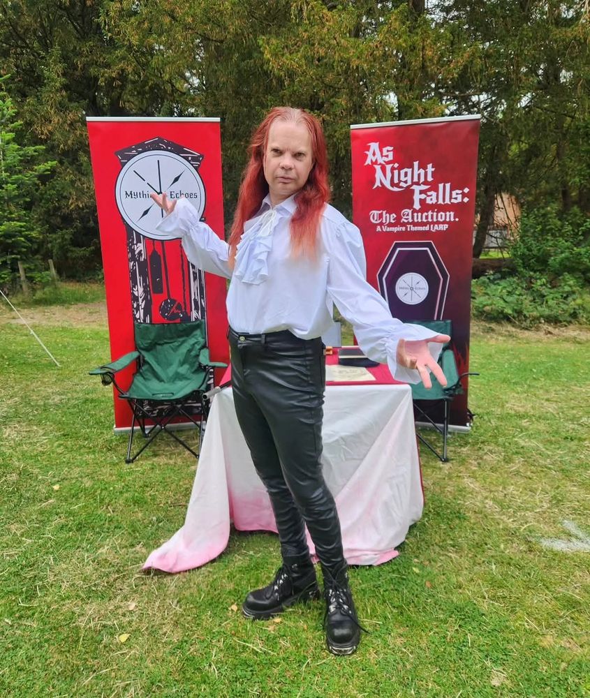Peter Ray Allison in white ruffled shirt and black leather leggings standing in front of the Mythic Echoes stand.