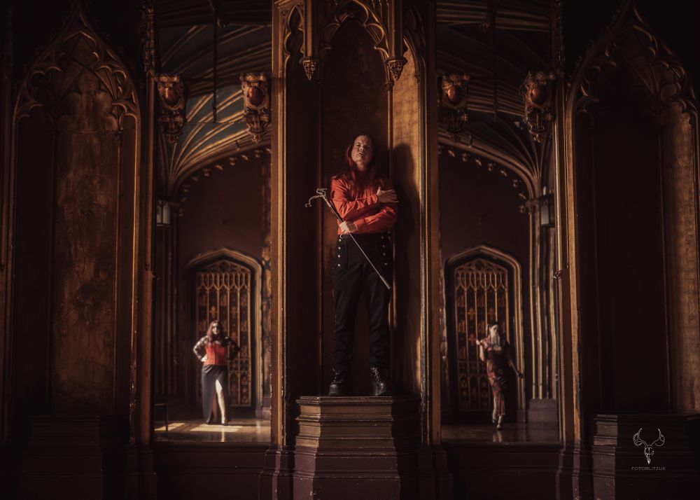 A male vampire on a stand flanked by two female vampires reflected in mirrors. 