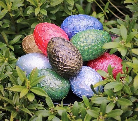 A cluster of multicolored dragon eggs in lavender, red, green, gold, bronze, and blue are nestled amid greenery. AltTxt by JS Crail.