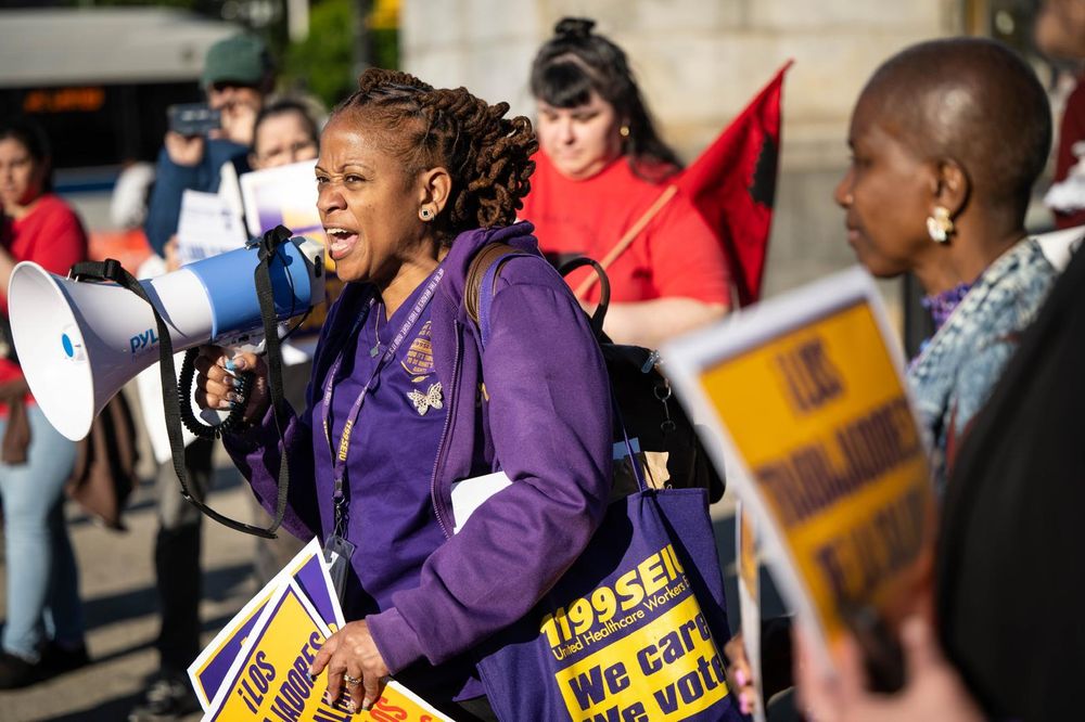 Members of SEIU local 1199  speaking into a megaphone at a rally  demanding the release of farm workers detained by ICE earlier this month