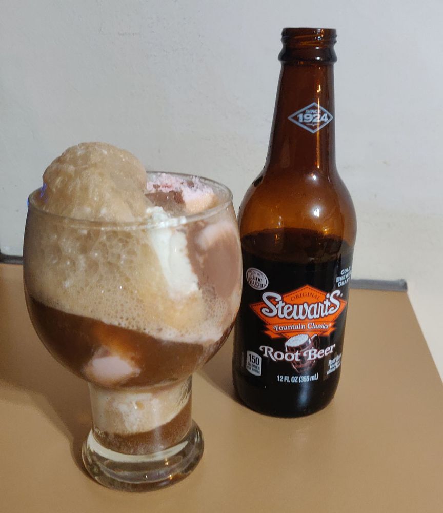 A beer glass filled with ice cream and and root beer, and a bottle of root beer soda.