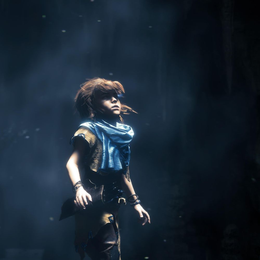 A young Aloy is in a dark underground ruin, looking up where the light peaks through from the surface.