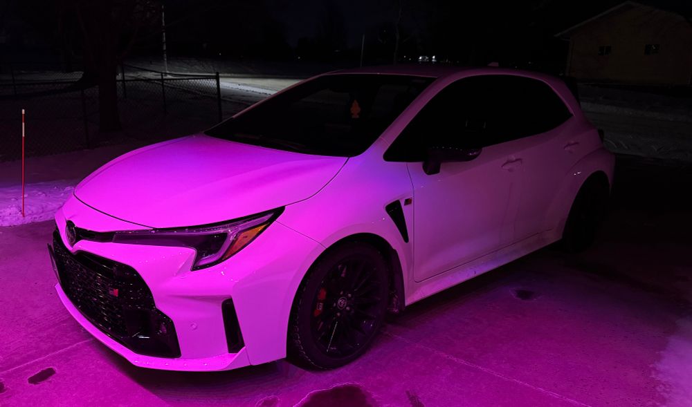 GR Corolla in white at night with pink lights shining on the hood. 