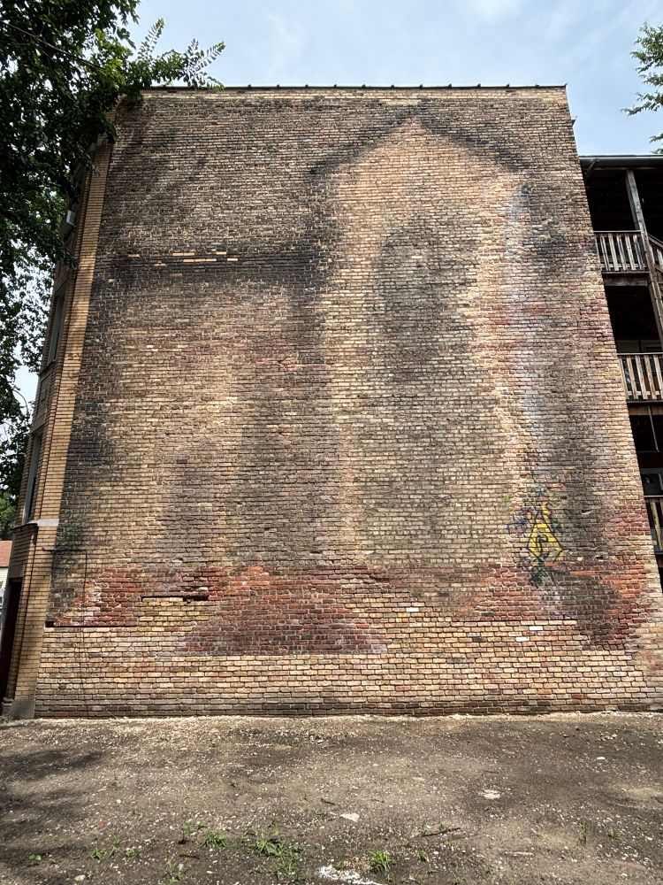The grimy outline of a home can be seen on a large, windowless brick wall
