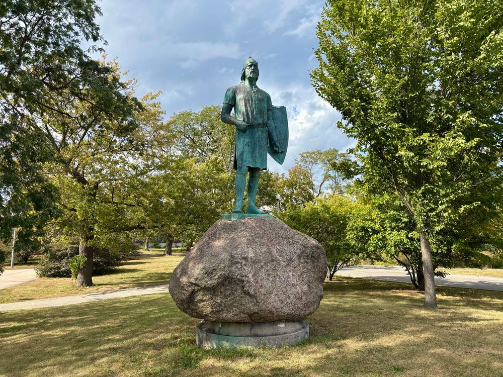 A  rinse statue of Leif Erickson atop a large granite boulder in a park