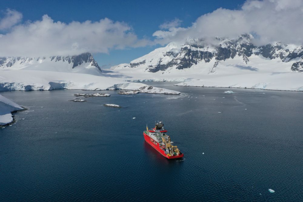 A ship on a flat ocean with snow covered mountains in the background