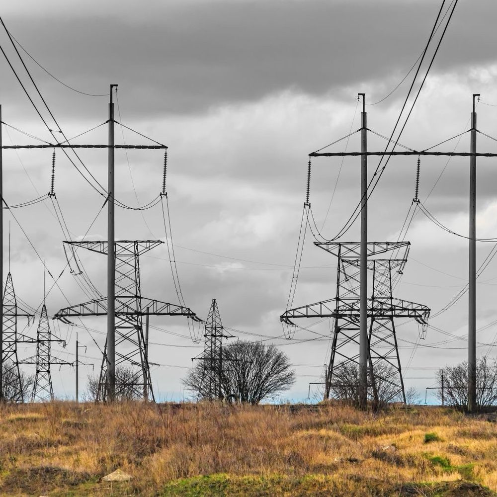 high tension transmission lines over an empty field, beneath a dark cloudy sky