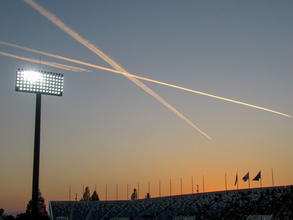 熊谷ラグビー場の夕景。日が暮れて照明灯がついている。飛行機雲が上空で交差している。