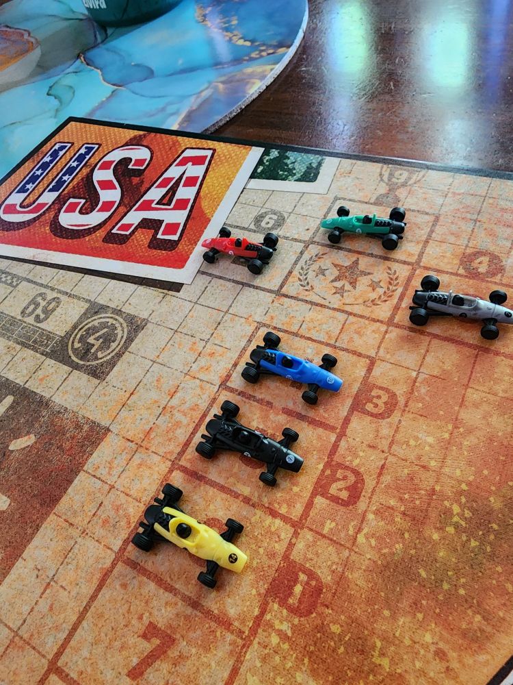The final race winners bracket in this solo game of Heat: Pedal to the Metal.  Green was in first place, followed by red in second and yellow in third.  The solo player, blue, ended in 4th.  Black and yellow ended Colin 5th and 6th place respectively.  The boardgame track used was the USA map depicted in bold red, white, and blue letters in the upper left corner.