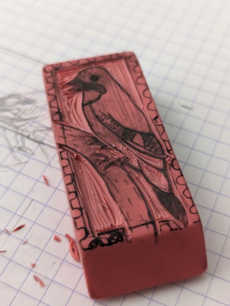 Photo d'une gomme rose en cours de gravure. Le dessin à sa surface est un oiseau (un geai des chênes) sur une branche.