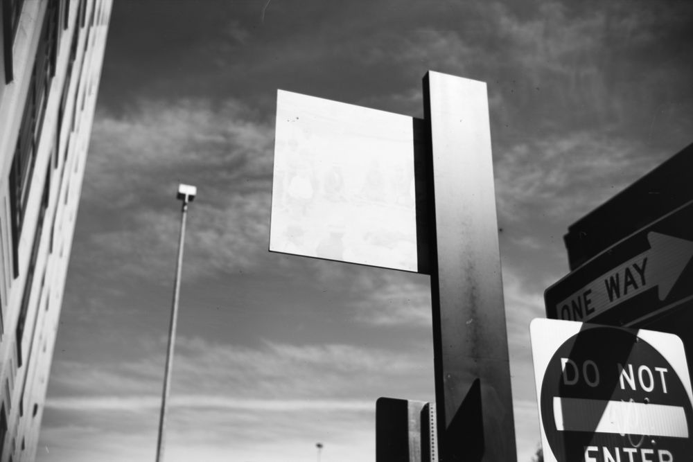 black and white photograph of street signs, street lights, building and sky.