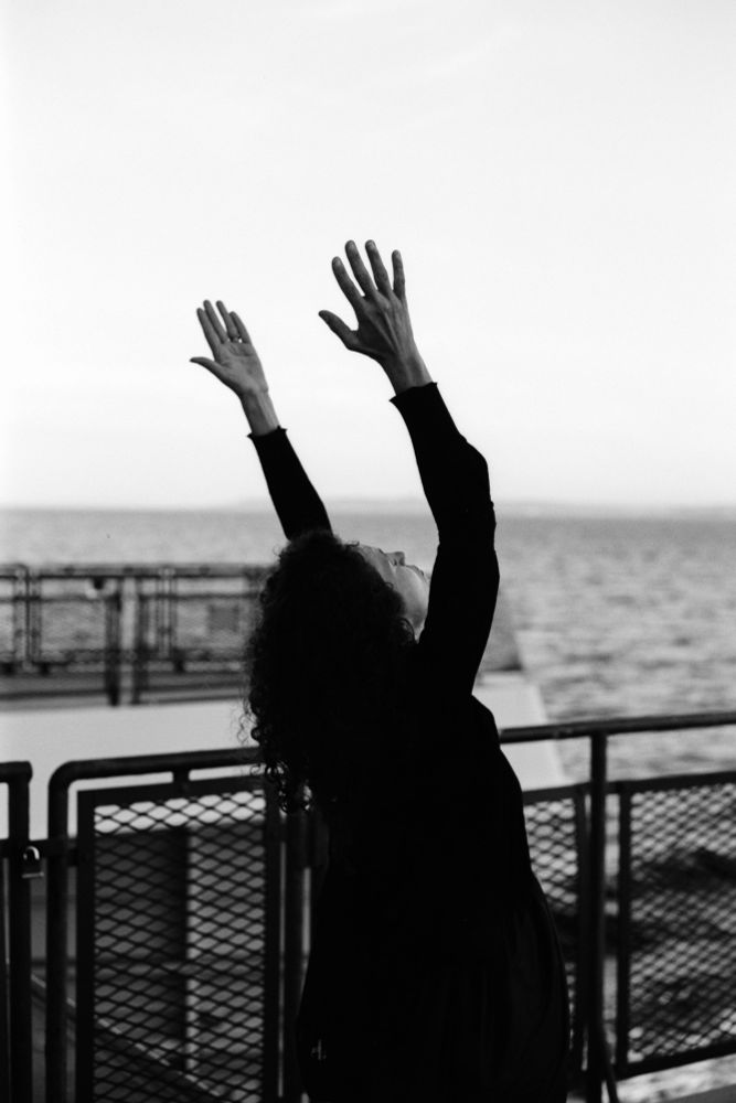 person on ferry with eyes closed and arms stretched up to the sky