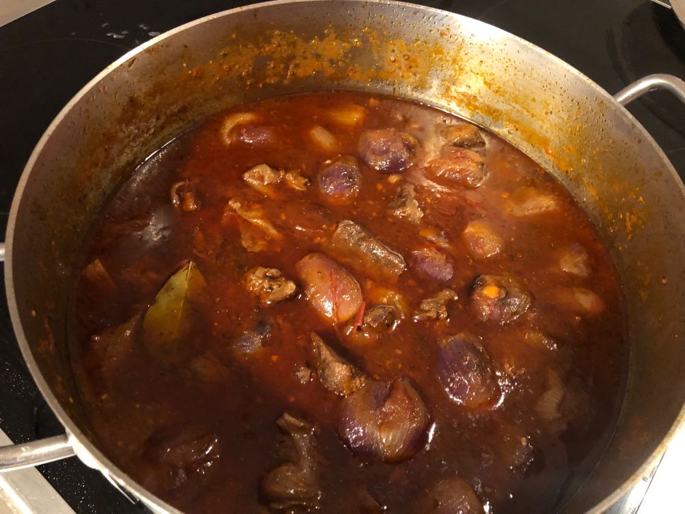 topf mit rotem saft,   fleischstücken und kleinen ganzen zwiebeln 