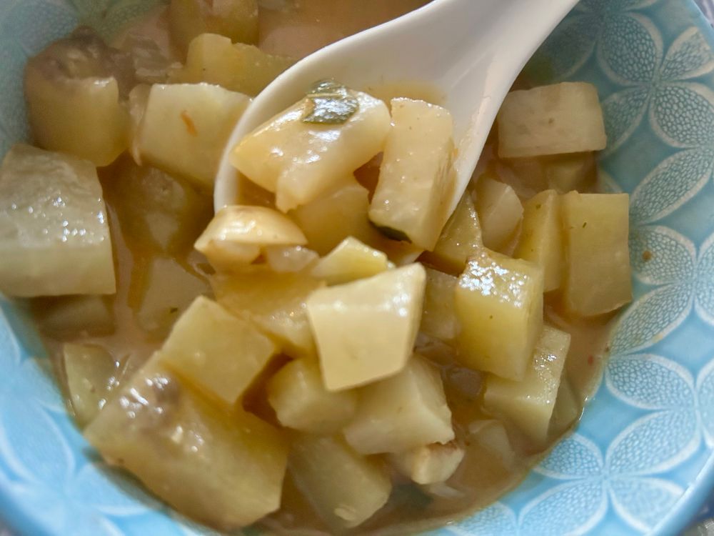 Kartoffelcurry in hellblauer Schüssel mit Keramiklöffel
