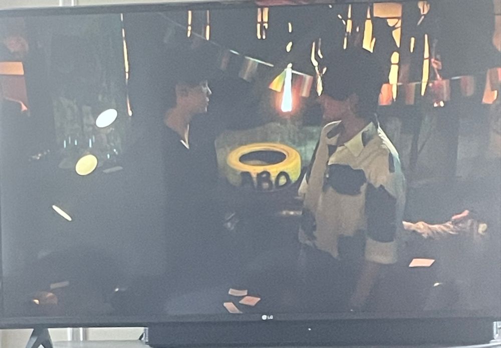 Two characters are talking in revenged love, behind them is a yellow tire, good sized, spray painted with ABO in black. There’s also a nice little banner of pride flags hung up like we’re at a pride party instead of an underground snake fight