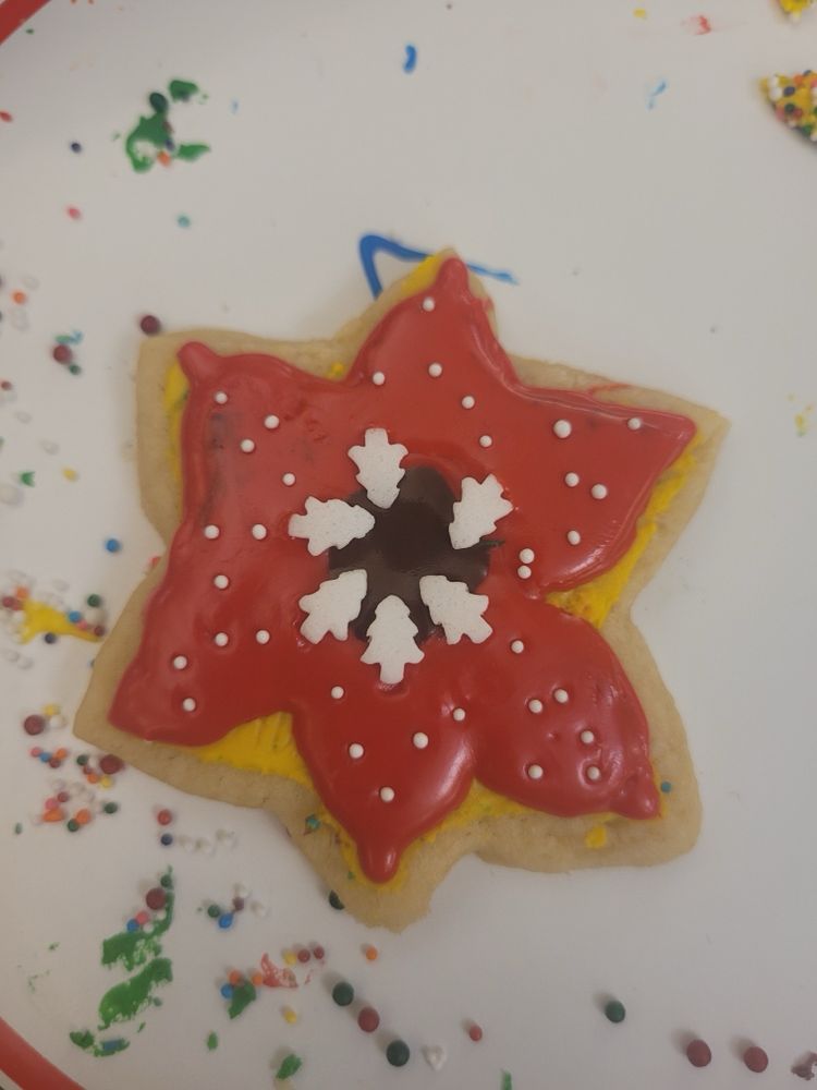 A sugar cookie cut out with a flower or maybe Star of David shape, frosted red with a black middle and white candy spikes. 