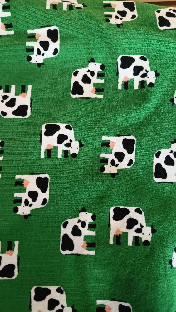 A close-up of the fabric, with a bright green background scattered with grazing black and white cows with pink udders. They all look the same, but are oriented differently along right angled axes.