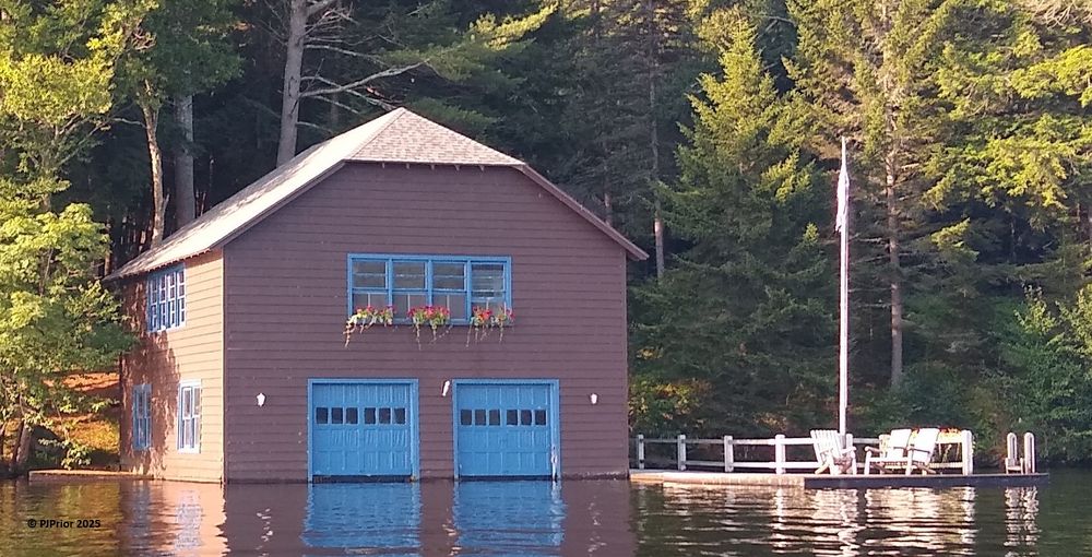 A brown boathouse with a dock and flowers on Fourth Lake, New York in July 2025.