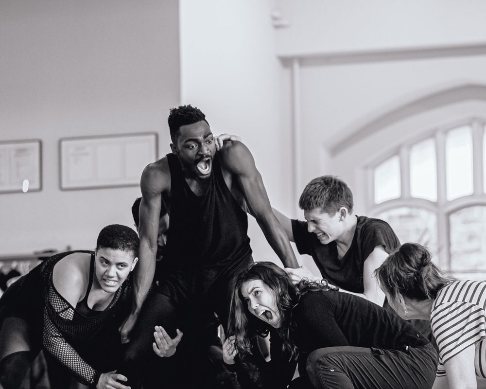 photo of an actor playing Oberon pulling themselves out of a crowd of fairies. actors wearing rehearsal clothing. expressions and bodies from the fairy world