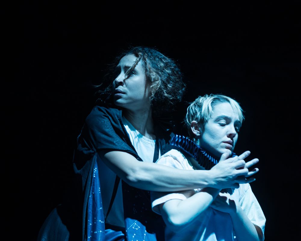 Photo is a woman in a cape waking up a woman in an Elizabethan ruff. Blue light. Magic. A spell.