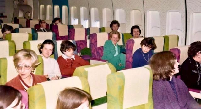 view of coach seats on a 1970's plane. Seats are magenta or lime green but spacious.