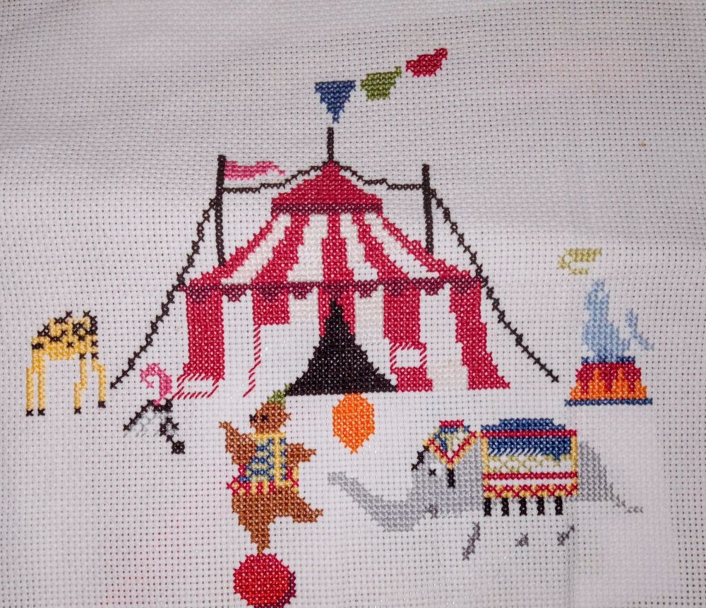 Circus Comes to Town by Tiny Modernist has most of a red and white striped circus tent with one pink flag and some pennants flying. Also a yellow and black giraffe's body with no head, a zebra's head with no body, but a pink feather on it's head, a pretty complete brown bear in a colored vest dancing on a red ball, an elephant with no legs holding an orange balloon and wearing a blue and red tassled blanket, and a ghostly gray seal on a red and orange stand balancing a yellow crescent that will be a ball on its nose.
