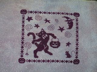 "Tom's Trick or Treat" by Waxing Moon Designs.  A dark purple cat is trick or treating with a pumpkin bucket while a rat and the moon look at him and a spider spins a web. Stitched on 18 ct lavender crystal Aida.