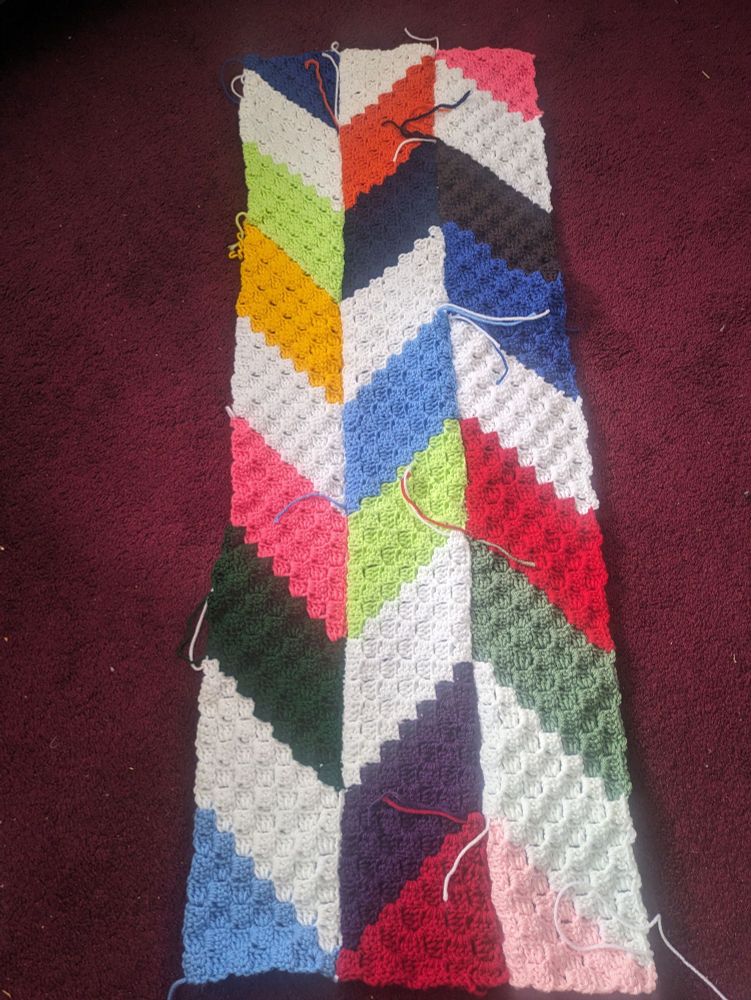 Crochet scrap blanket. Three strips in a chevron pattern - multi-coloured with blue, orange, yellow, white, pink, red, purple.
