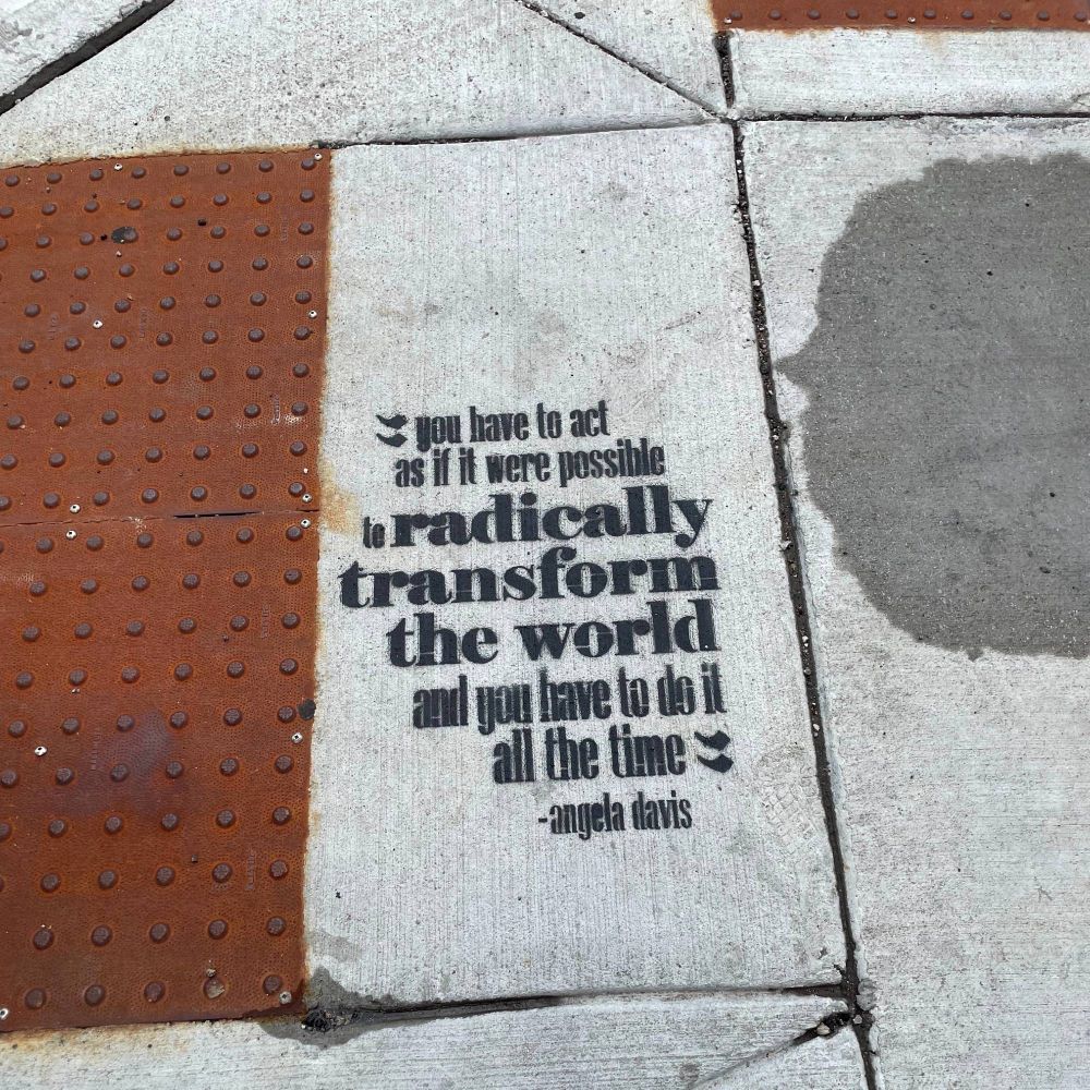 graffiti on the sidewalk says “you have to act as if it were possible to radically transform the world and you have to do it all the time” angela davis