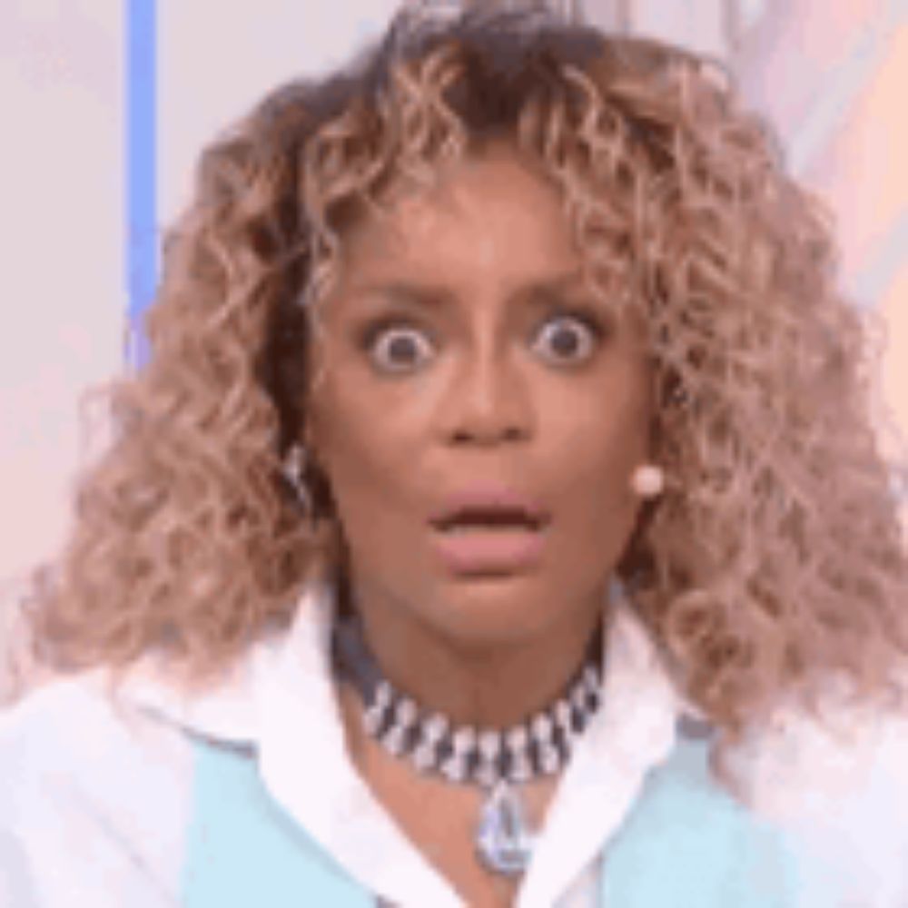 a woman with curly hair is making a surprised face while wearing a necklace .