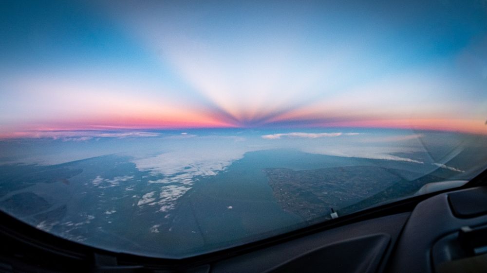 The UK east coast under converging blue shadow rays in a salmon and orange sky in this cockpit view