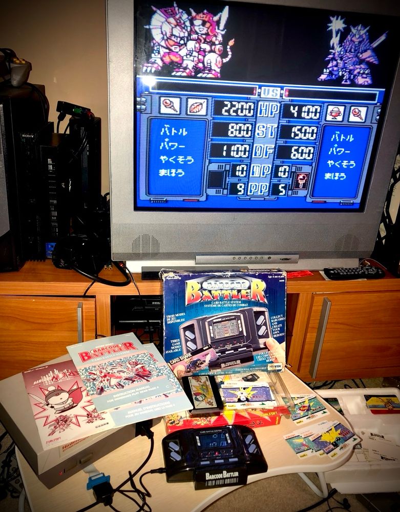 Barcode Battler II along with Famicom game and adapter running on a NES (with EXP and cart adapters). Instructions and cards scattered about with the game running on a CRT TV.
