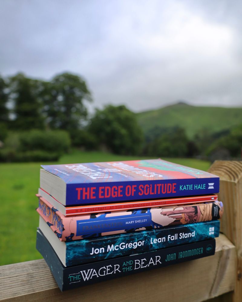 Book stack on gate in front of field and green fells under grey sky 