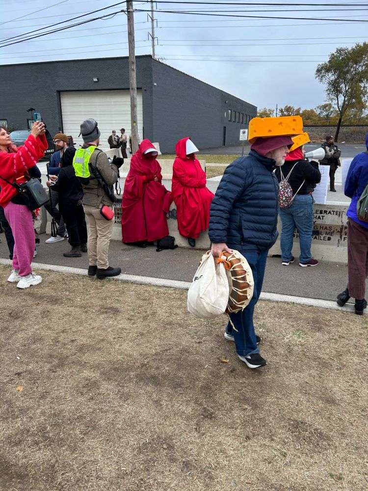 Protestors at Broadview ICE include two women dressed as handmaidens from The Handmaid's Tale, all in red with white bonnets. To the right are two people from Wisconsin (I think) wearing the tradition headgear, a giant wedge of cheese. photo taken Nov. 8
