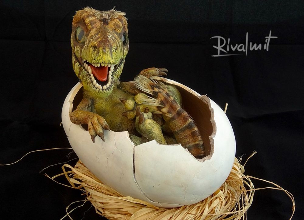 A sculpture of a little dinosaur, just hatched, sits in  open-cracked egg. The dinosaur is green-orange-braun colored with scales and feathers