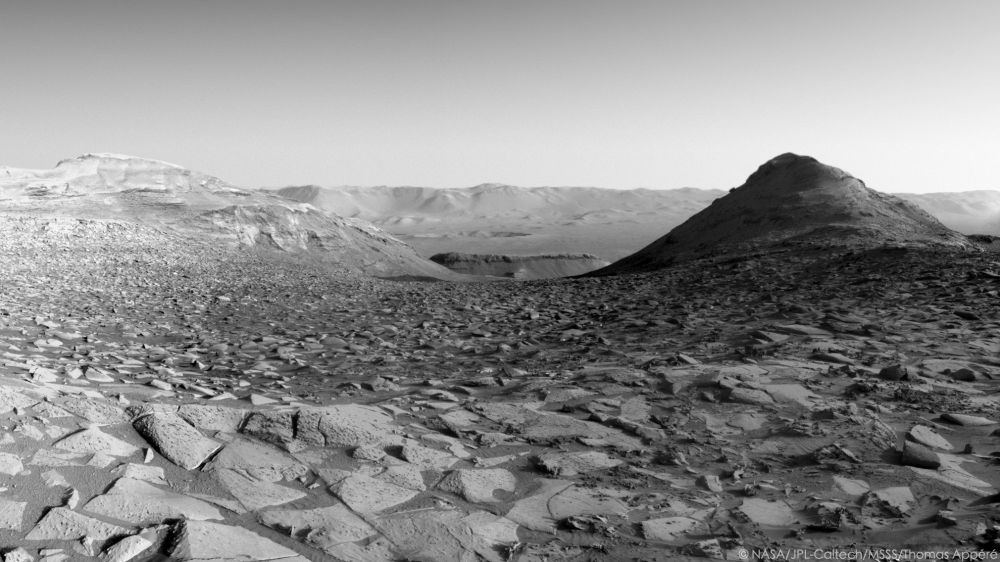 Cette vue a été acquise par la caméra de navigation NavCam Right du rover martien Curiosity au sol 4505, le 8 avril 2025, à 7h10 heure locale. La colline à droite, dont un flanc est plongé dans l'ombre, a été baptisée Gould Mesa. Elle est haute de 30m. Au loin, on distingue clairement le rempart du cratère Gale grâce à la faible opacité de l'atmosphère en cette saison.