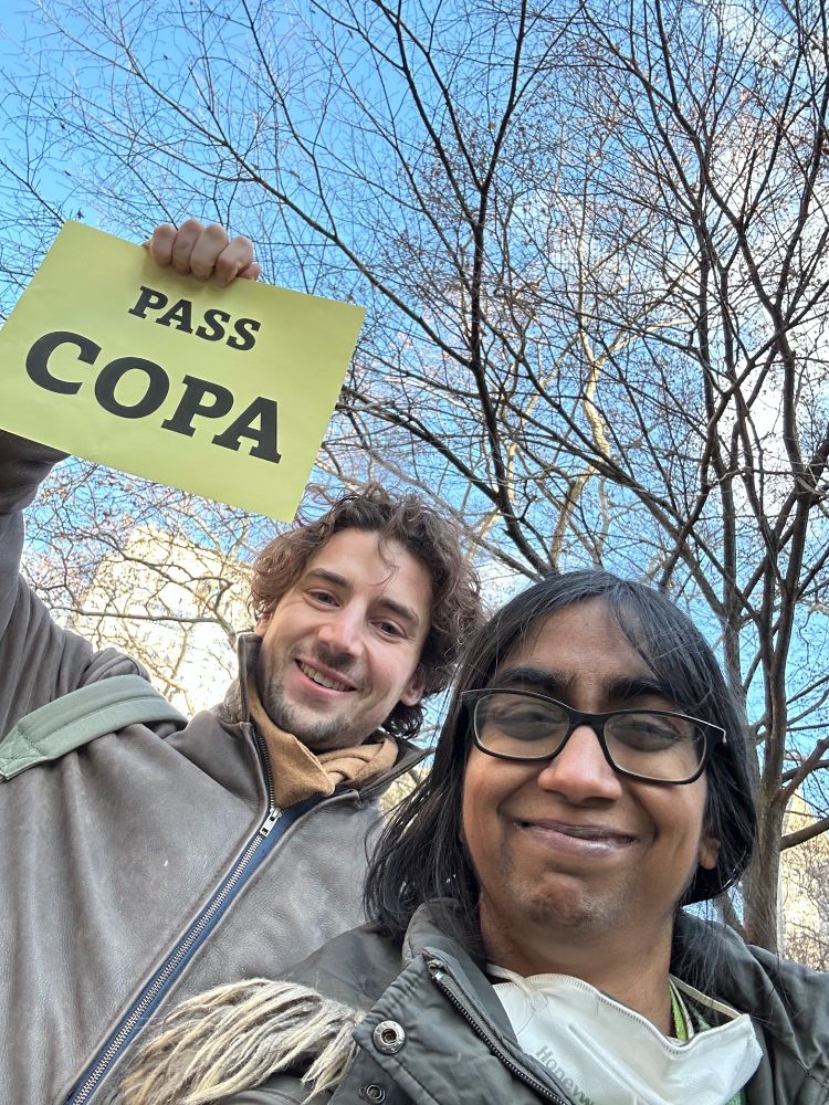 Two people pose for a selfie, one holding a yellow sign that says PASS COPA