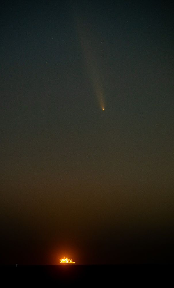 The comet about 20° above the horizon and just slightly to the right of an oil drilling platform in the Pacific Ocean
