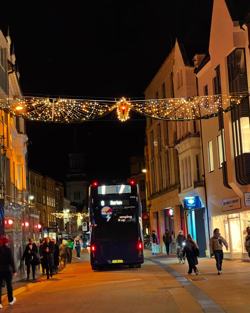 An electric bus and a few people walking on a street lit with the Christmas and new year decorations. 