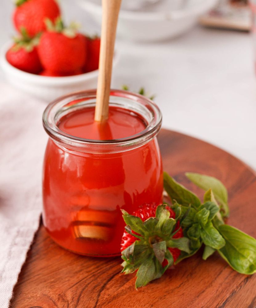 strawberry basil simple syrup in glass jar with honey dipper resting in jar and a strawberry top and basil resting against the side