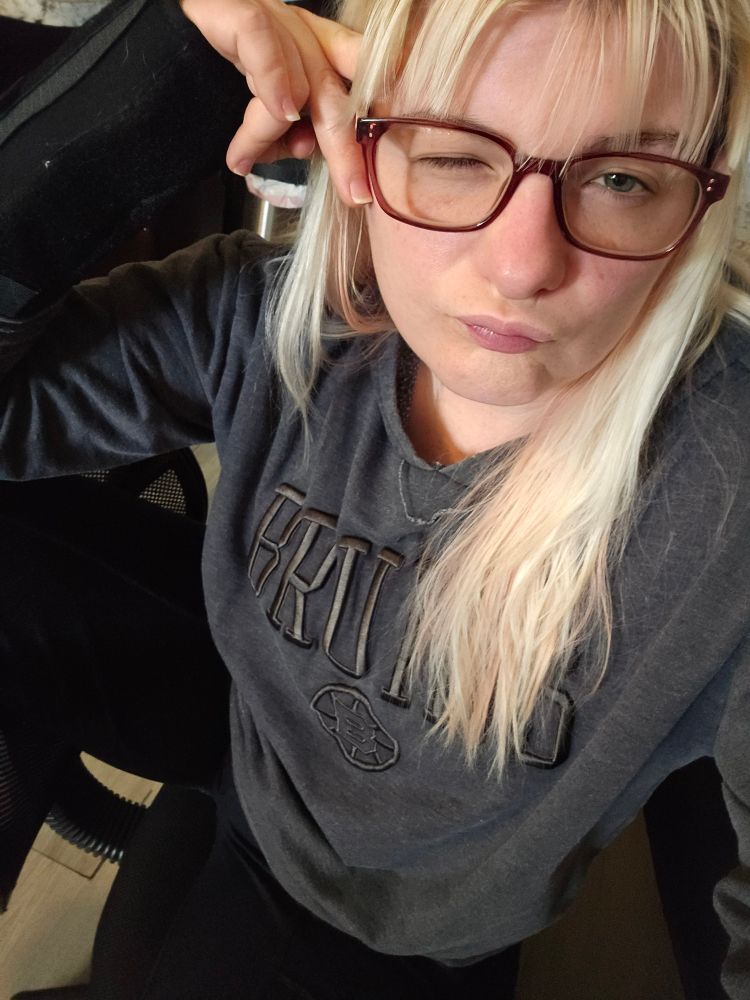 Duck lipped peace signing loser sits w their leg over the back of an office chair, the other off the seat end. The hoodie in question is dark gray, with BRUINS written in a slightly darker gray 3D patched letters the spoked B sits just below it. 