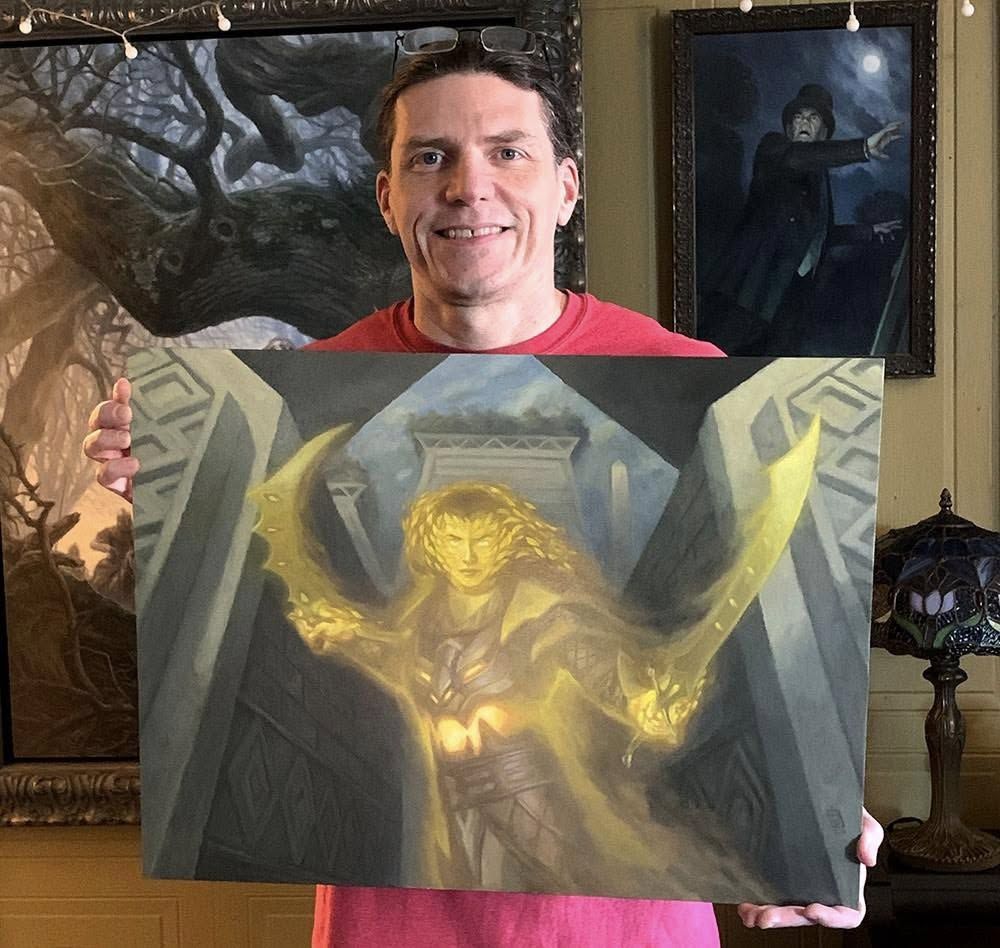 artist matt stewart holds a painting of a lady with two swords in his hands. The lady in the painting is glowing yellow and looks pretty fierce