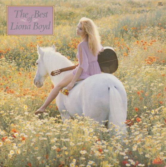 Liona Boyd holding a guitar and riding a white horse through a field of flowers